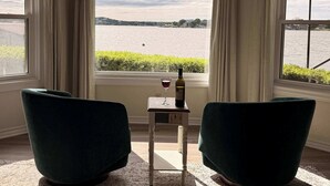 A room with a view of a body of water, two chairs, a small table with a wine bottle and glass, and a window with curtains. - 75' Amazing Lake View   Dock   Pets  Gameroom (Granite Shoals)