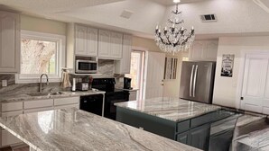 A modern kitchen with white cabinetry, a marble countertop, a stainless steel refrigerator, and a chandelier. - 75' Amazing Lake View   Dock   Pets  Gameroom (Granite Shoals)