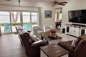 A living room with a large window, a sofa, a TV, and a dining area. - 75' Amazing Lake View   Dock   Pets  Gameroom (Granite Shoals)