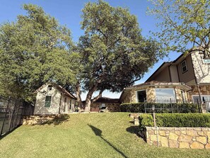 A residential area with two houses, one with a stone facade and the other with a wooden exterior. There is a well-maintained lawn and a large tree providing shade. - 75' Amazing Lake View   Dock   Pets  Gameroom (Granite Shoals)