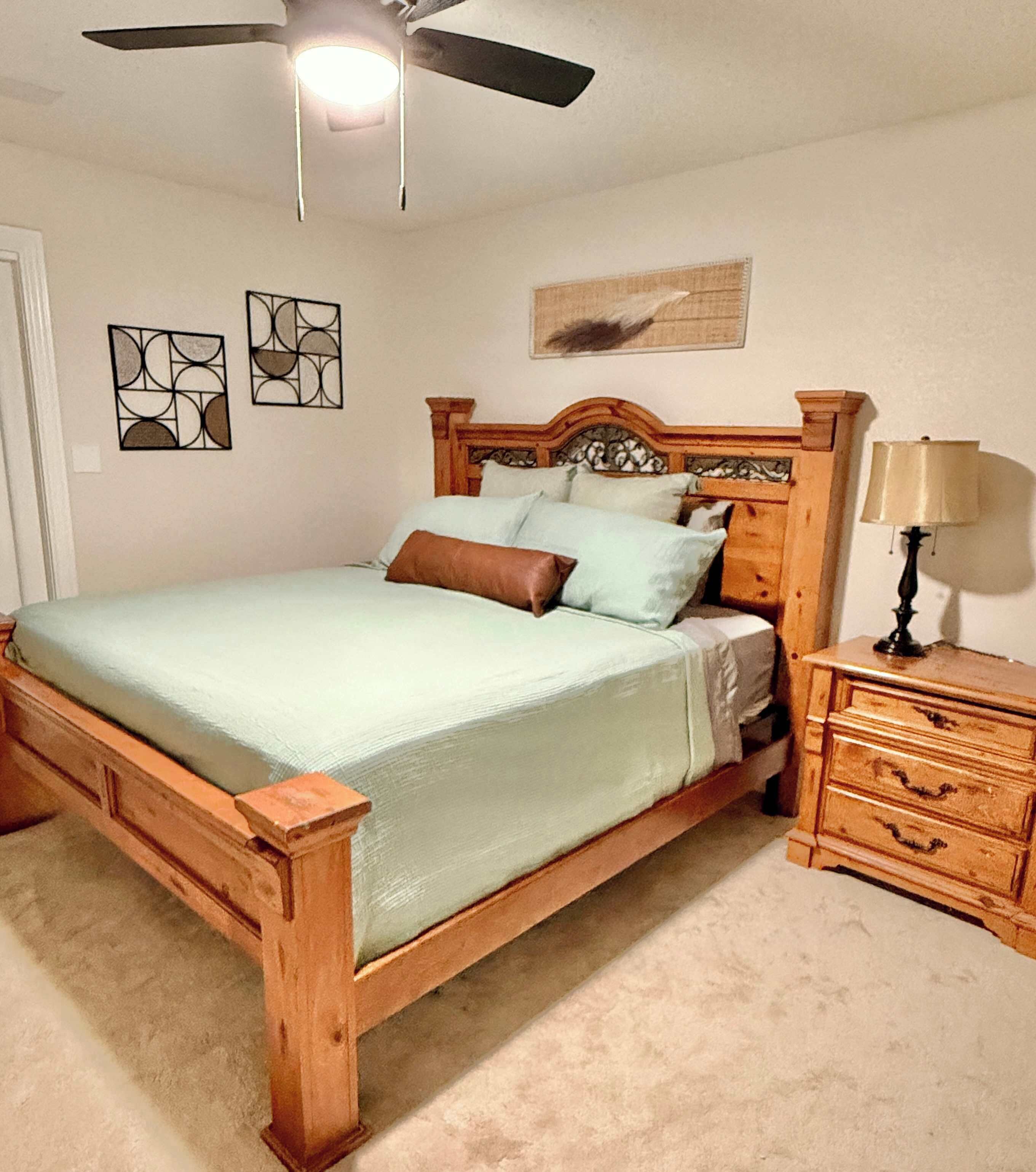 A bedroom with a wooden bed, a nightstand, a lamp, and two wall art pieces.
