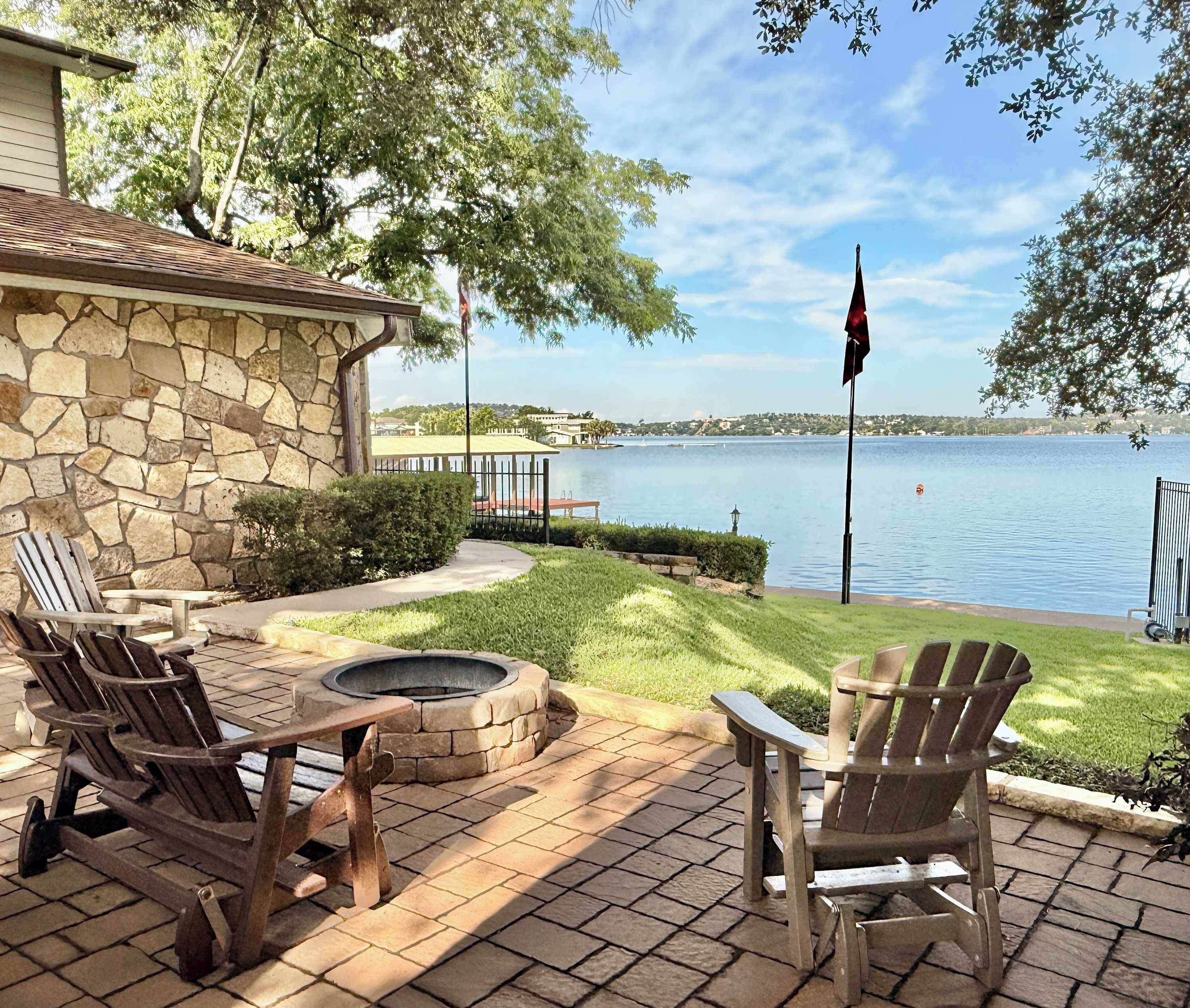 A patio with stone walls, a fire pit, and Adirondack chairs overlooking a lake.