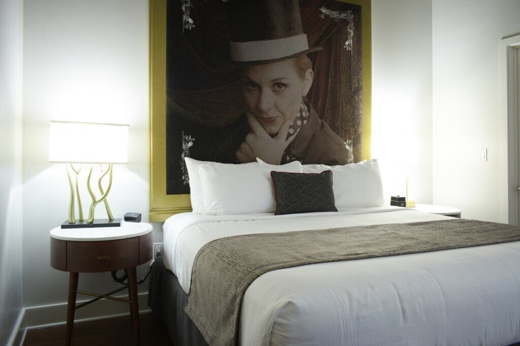 A hotel room with a bed, a bedside table with a lamp, and a large poster on the wall.
