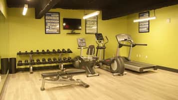 Ein Fitnessraum mit Trainingsgeräten, darunter Kurzhanteln, eine Bank, ein Laufband und ein Crosstrainer.