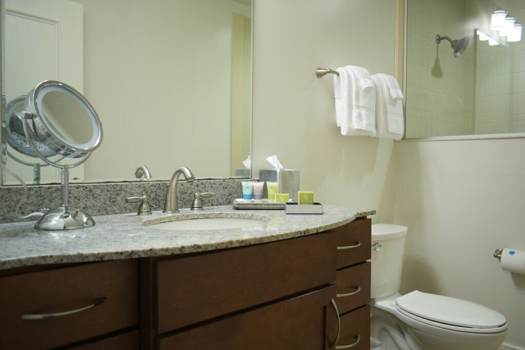 A bathroom with a sink, mirror, toiletries, and a toilet.