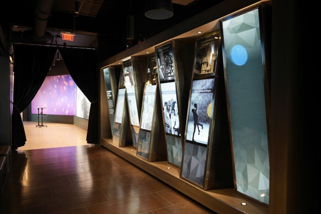 Un passadís amb panells expositius, una paret il·luminada de morat i un senyal de sortida.