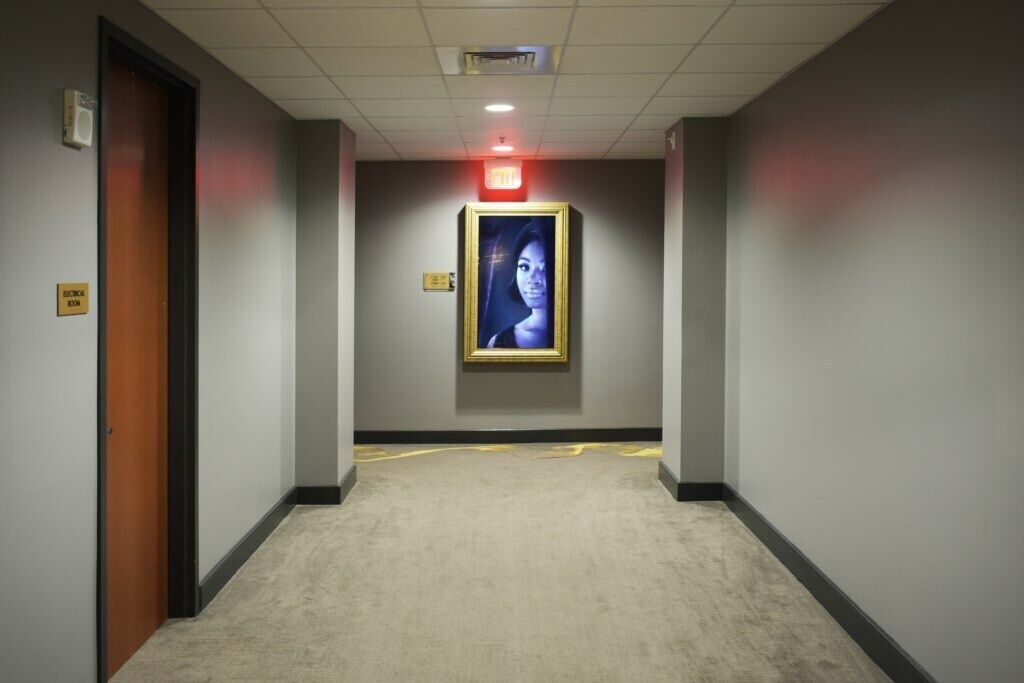 Un couloir doté d’un sol recouvert de moquette, d’un tableau encadré accroché au mur et d’une porte portant l’inscription « Salle de biologie », située sur le côté gauche.