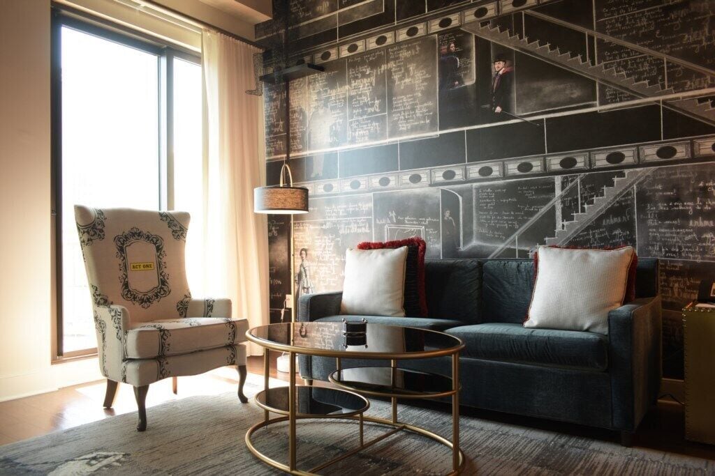 Een kamer met een blauwe bank, een gestreept fauteuil, een klein rond tafeltje en een wand bedekt met een schoolbord met teksten.