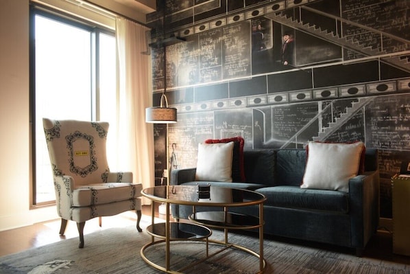 A room with a blue sofa, a patterned armchair, a small round table, and a wall covered in chalkboard with writings.