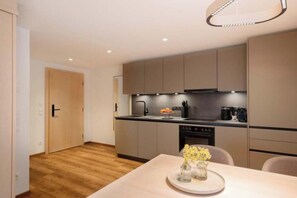 A modern kitchen with a dining area, wooden flooring, and a small table with a vase of flowers. - Tafamunt 11 Apartment (Gaschurn)