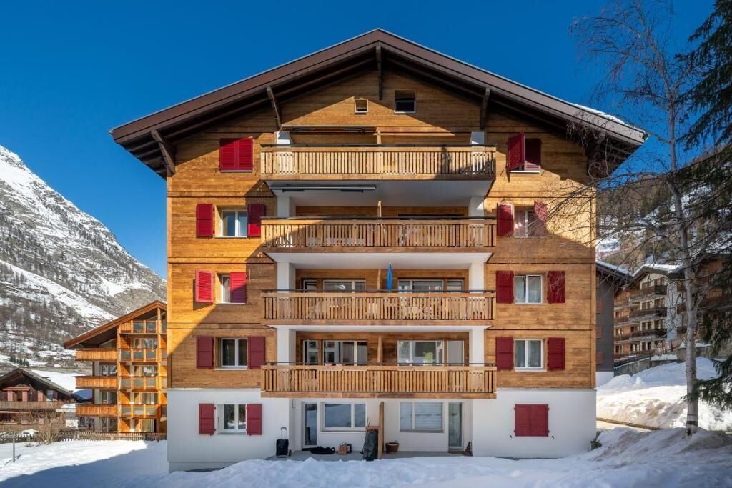 A multi-story wooden building with balconies, set against a snowy mountain backdrop.