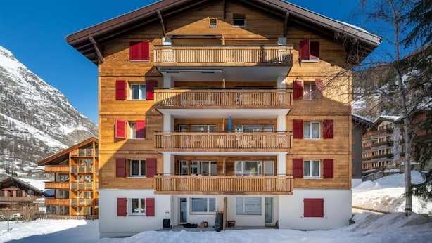 A multi-story wooden building with balconies, set against a snowy mountain backdrop. - Chalet Horu - By InspiringPlaces (Zermatt)