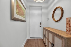 Ein Korridor mit einer weißen Tür, einem gerahmten Bild an der Wand, einem Holzschrank und einem gewebten Korb.