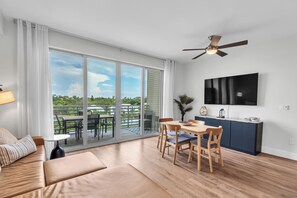 Un salon moderne comprenant un canapé, une table à manger et des chaises, un ventilateur de plafond et un téléviseur fixé au mur.