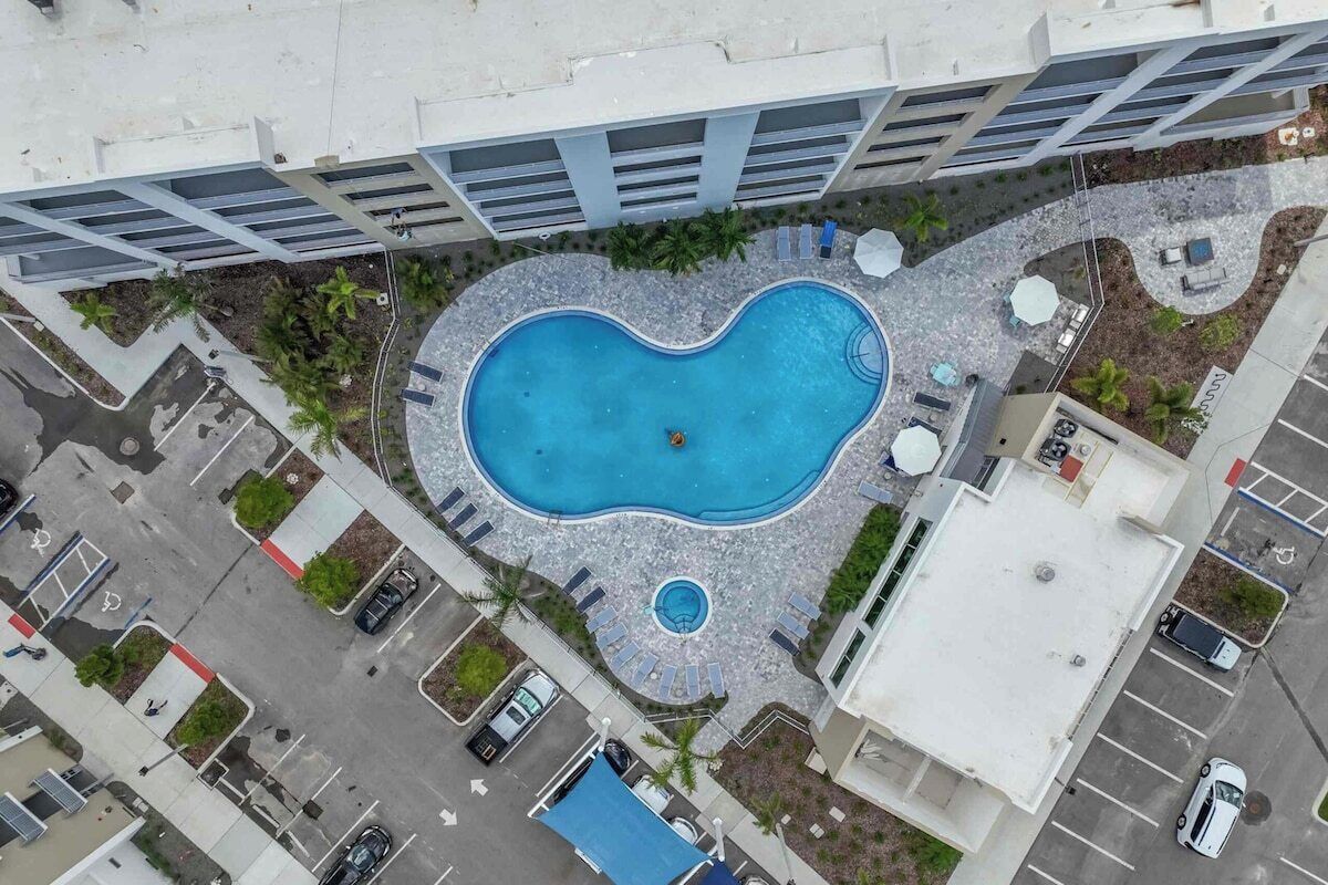 Vista aèria d'un edifici amb piscina, zona d'aparcament i vegetació als voltants.