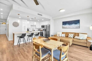 Une cuisine moderne avec des meubles blancs, un îlot central doté de tabourets de bar et un coin repas avec une table et des chaises en bois.