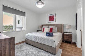 Ein Schlafzimmer mit Bett, Nachttischen, einem Fenster, einer Deckenleuchte und einem gerahmten Bild an der Wand.