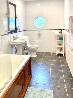 A bathroom with a bathtub, sink, toilet, and a small shelf with toiletries. - Oyster Cove Kilkerrin with stunning views (Kilkerrin)