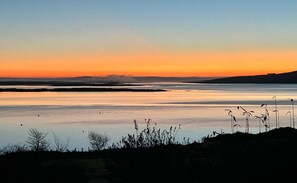 A calm lake at sunset with silhouettes of vegetation and distant hills. - Oyster Cove Kilkerrin with stunning views (Kilkerrin)