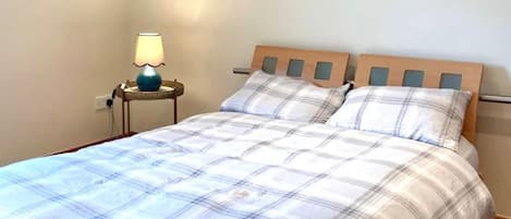 A bedroom with a bed, a nightstand with a lamp, and a wall socket.