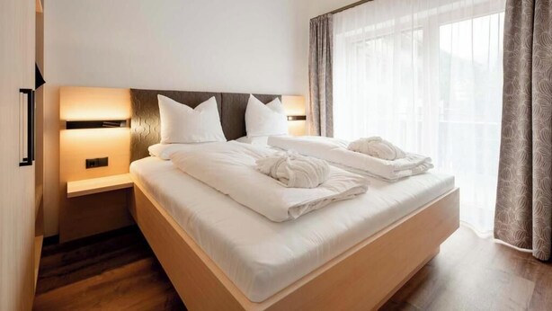 Habitació d'hotel amb un llit gran, tauletes de nit i vistes a través de cortines lleugeres.