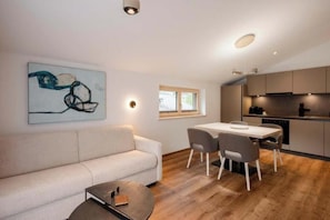 Ein modernes Wohnzimmer mit einer Couch, einem Esstisch mit Stühlen sowie einer Küchenzeile mit Schränken und Geräten.