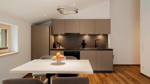 Cuina moderna amb zona de menjador, que destaca per una illa central amb fruita, il·luminació empotrada i vista a l'exterior.