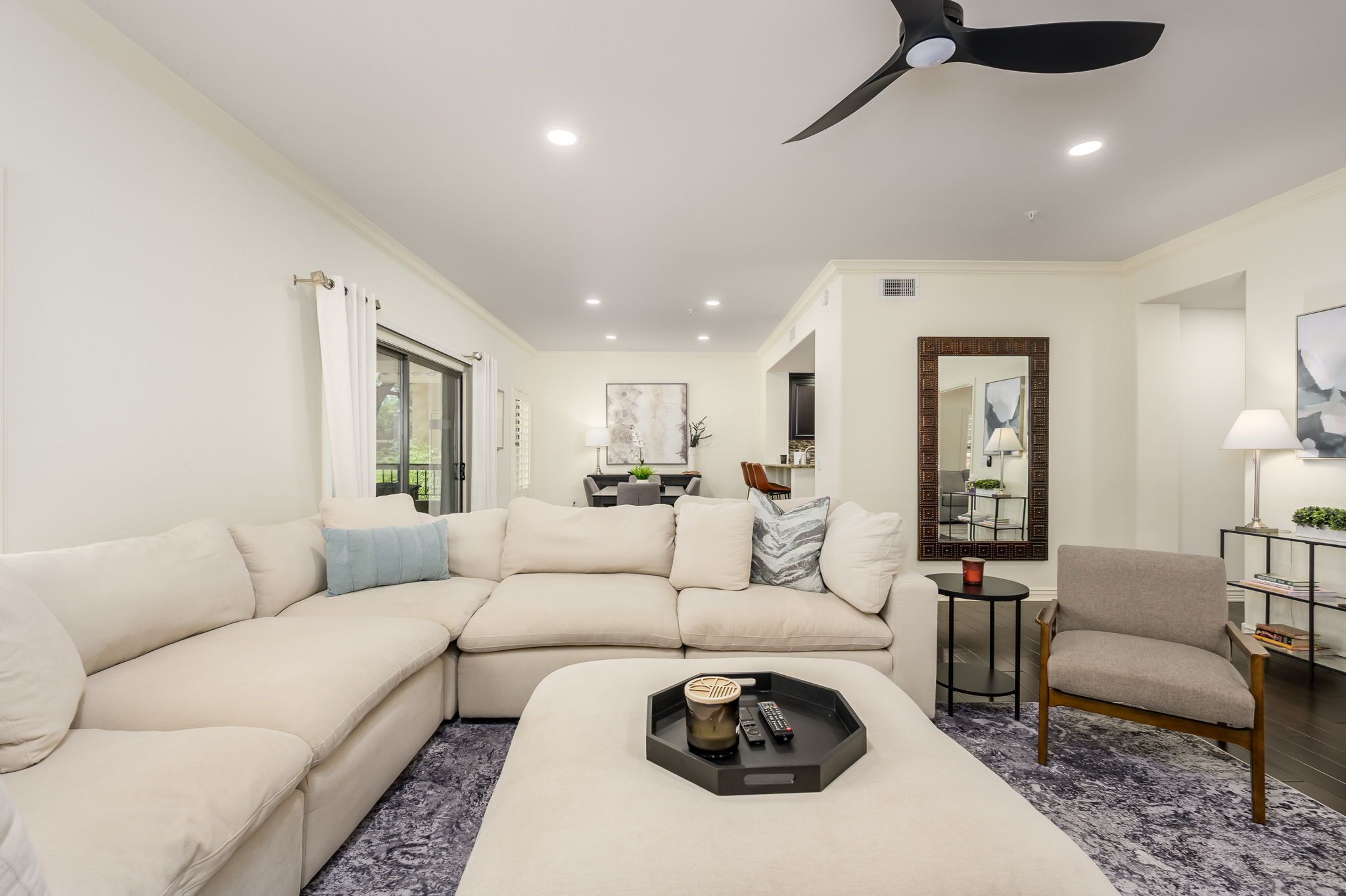 A modern living room with a sectional sofa, a coffee table, a side table, and a ceiling fan.