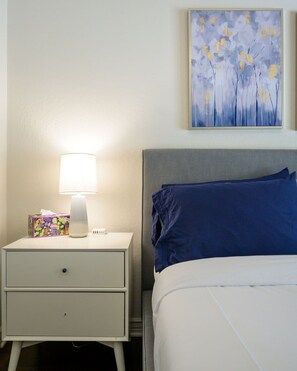 A neatly made bed with blue pillows, a bedside lamp, and a box of tissues on a white nightstand. - Highly desired Desert Ridge condo on 1st level- no stairs, large patio (Phoenix)