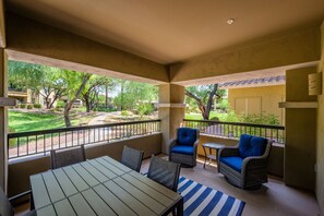 A covered outdoor seating area with a table and two chairs, a small table, and a view of a landscaped garden. - Highly desired Desert Ridge condo on 1st level- no stairs, large patio (Phoenix)