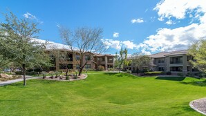 A residential area with a well-maintained lawn, mature trees, and two-story buildings with a Mediterranean architectural style. - Highly desired Desert Ridge condo on 1st level- no stairs, large patio (Phoenix)