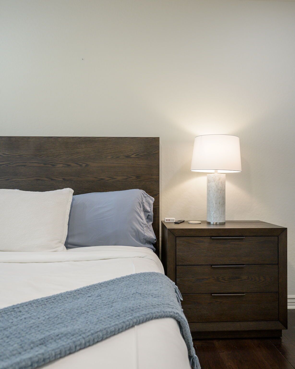 A bed with a wooden headboard, a bedside table with a lamp, and a blue throw blanket.