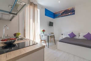 A modern hotel room with a kitchenette, a dining area, and a bed with purple pillows. - Lovely 22 sqm studio apartment, for two guests, located on the second floor of a renovated historic building (no elevator). The property enjoys a strategic location just steps away from the Policlinico hospital, the Ballarò district, and the city center (Palermo)
