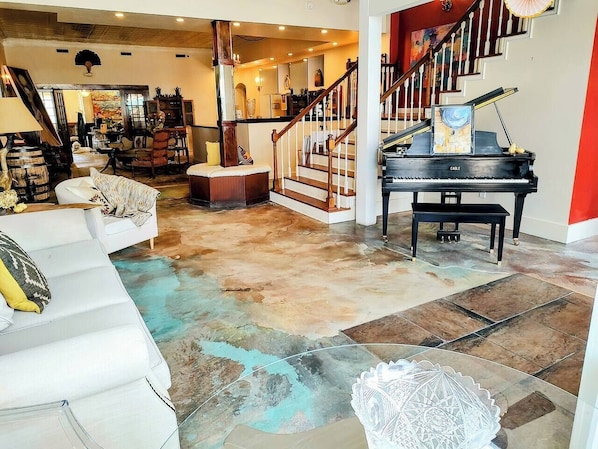 A spacious living room with a grand piano, a staircase, and a modern interior design.
