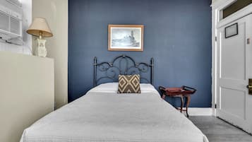 A bedroom with a bed, a framed picture on the wall, a bedside table, and a lamp.