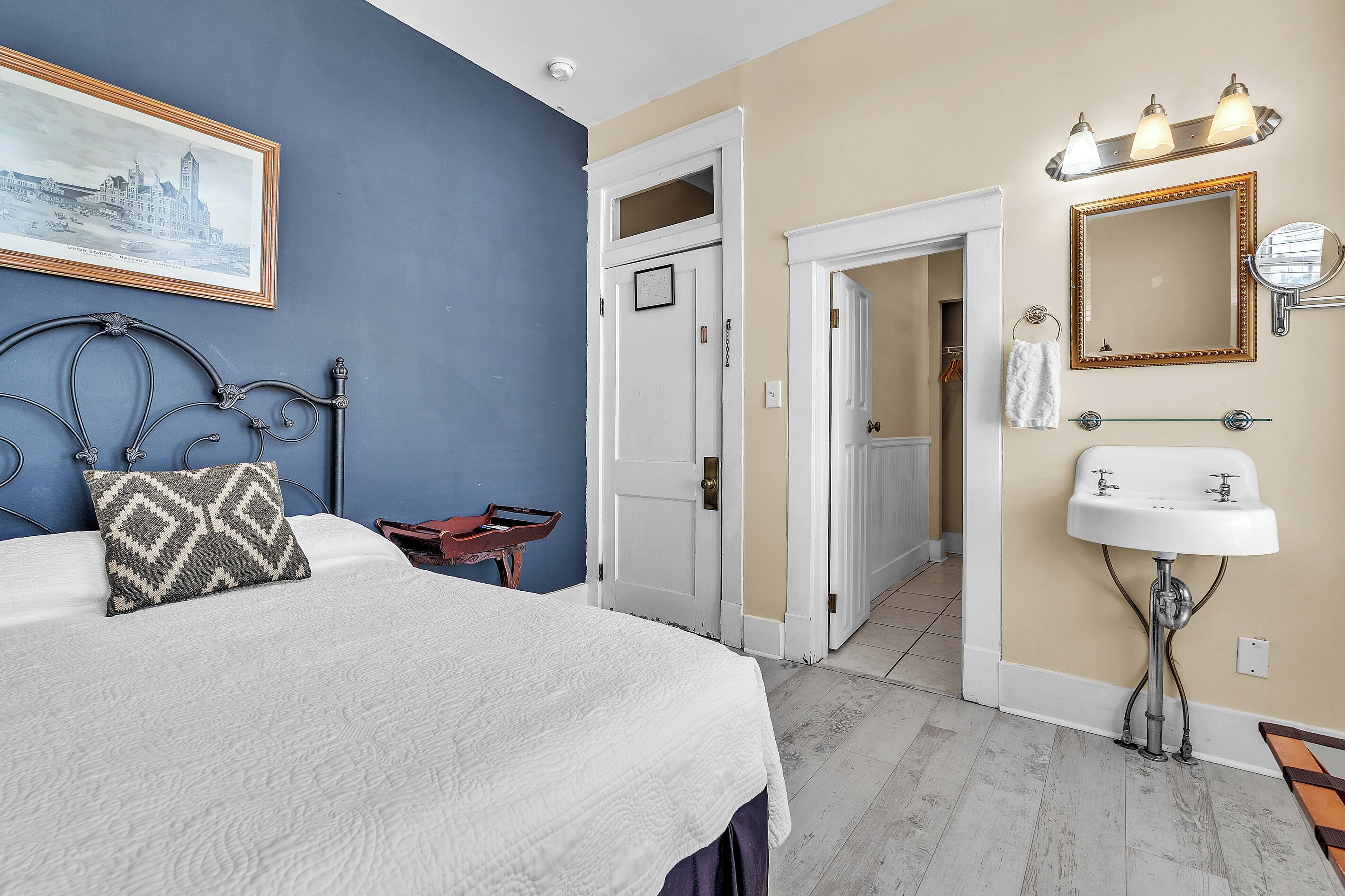 A bedroom with a bed, a nightstand, a dresser, a mirror, and a bathroom with a sink.
