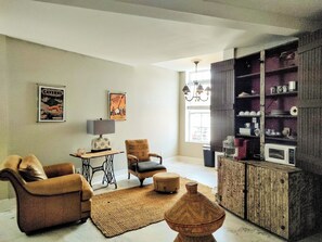 Ein Wohnzimmer mit Sofa, Sessel, Tisch, Lampe, dekorativer Vase und einem Schrank mit Regalen.