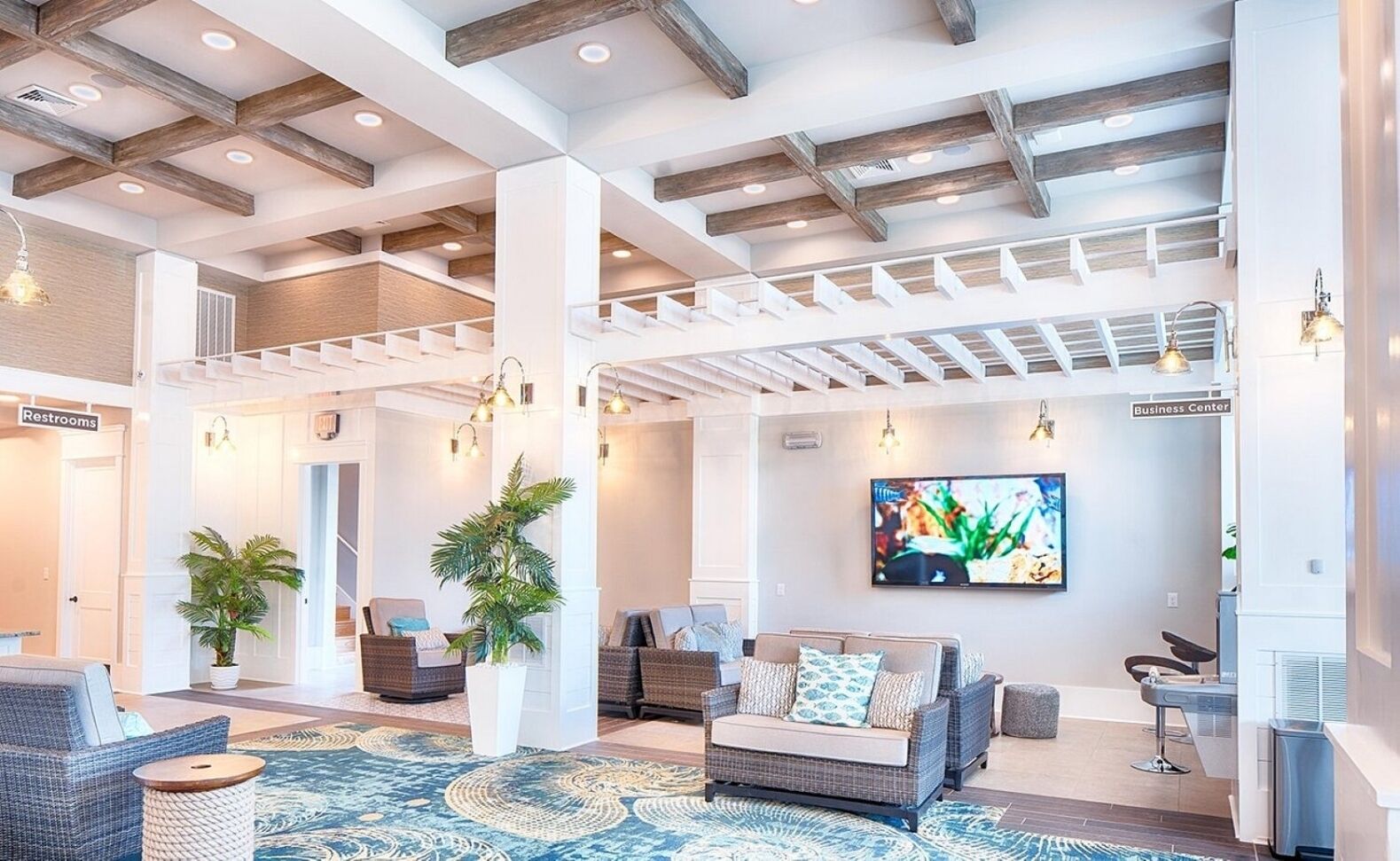 A spacious lobby with a high ceiling, wooden beams, a large TV screen, and a seating area with wicker furniture.