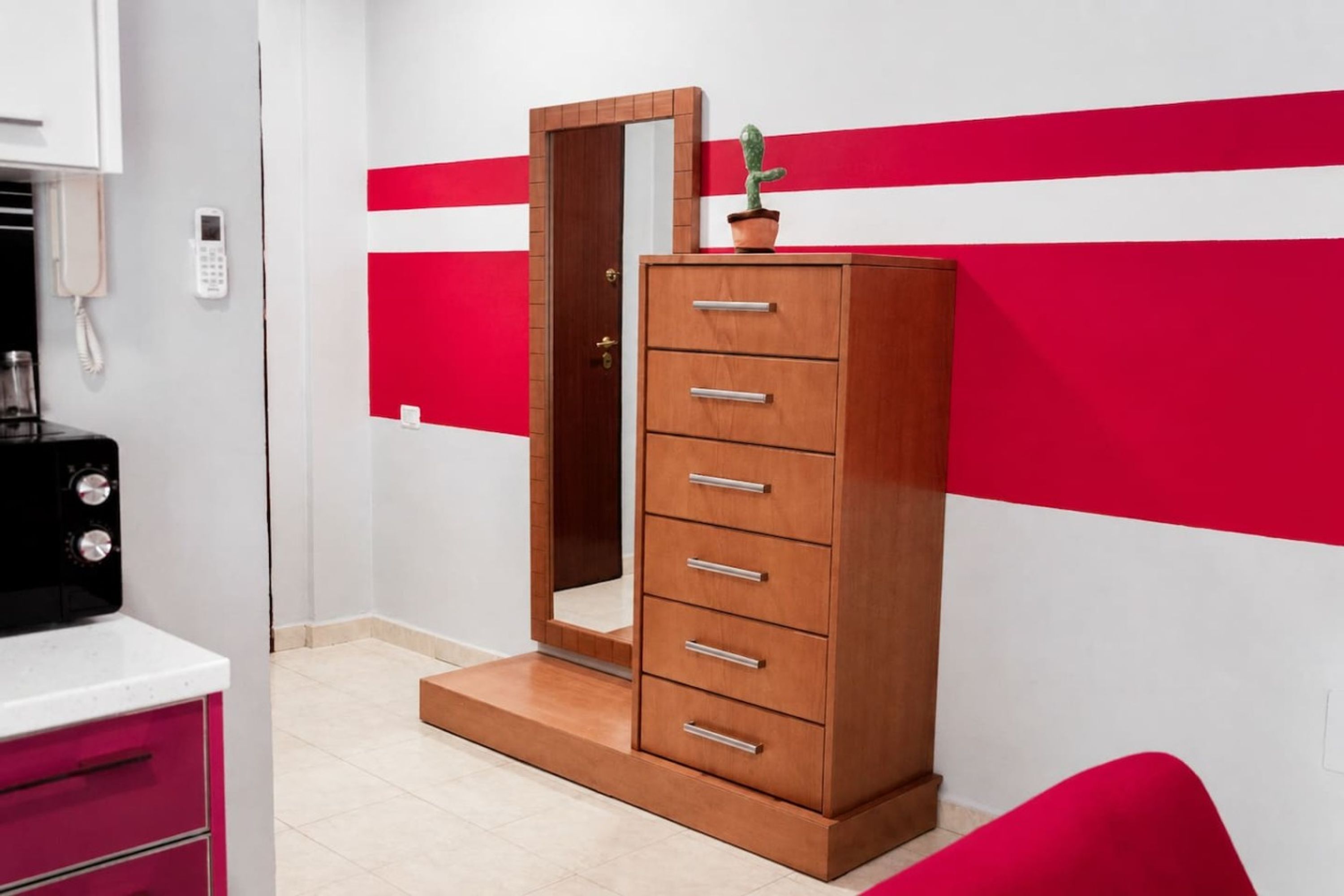 Une chambre avec une armoire en bois, un miroir, un téléphone et un motif mural rouge et blanc.
