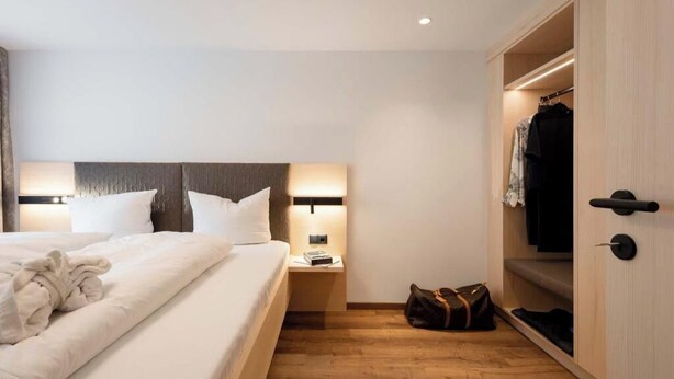 Habitación de hotel con cama, lámparas de noche, mesita de noche, bata, bolso y armario.
