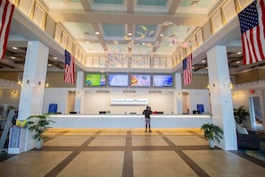 Área de recepção do Grand Palms Resort, com um balcão central, bandeiras americanas e telas digitais exibindo informações.