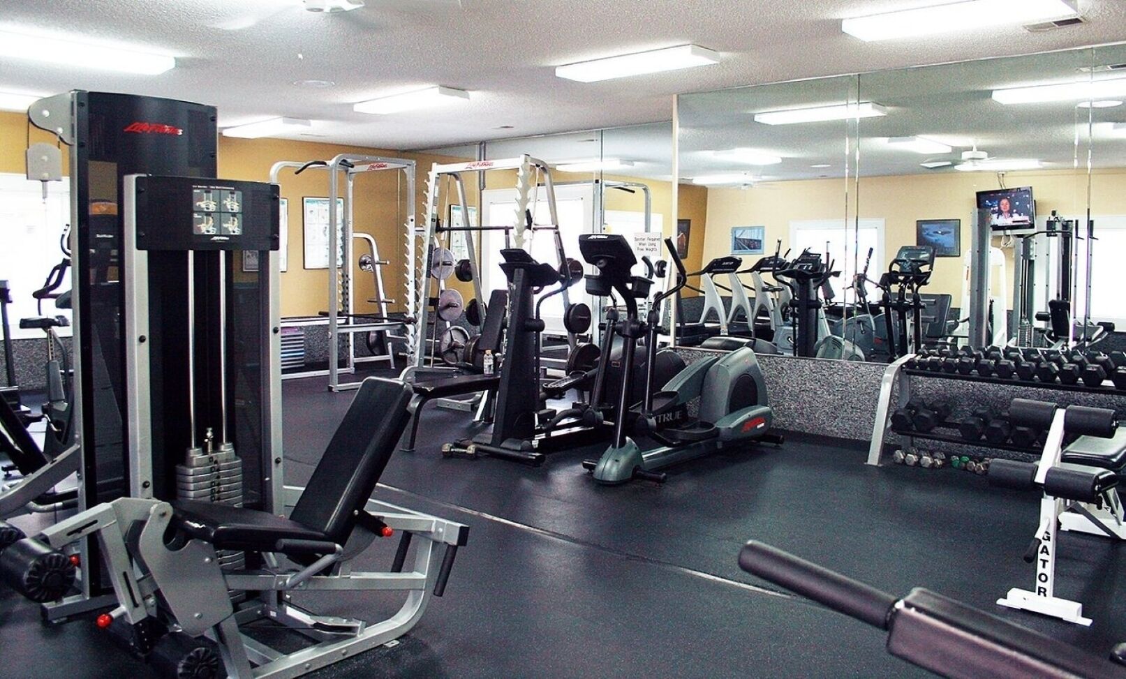 A gym with various exercise machines, mirrors, and weights.