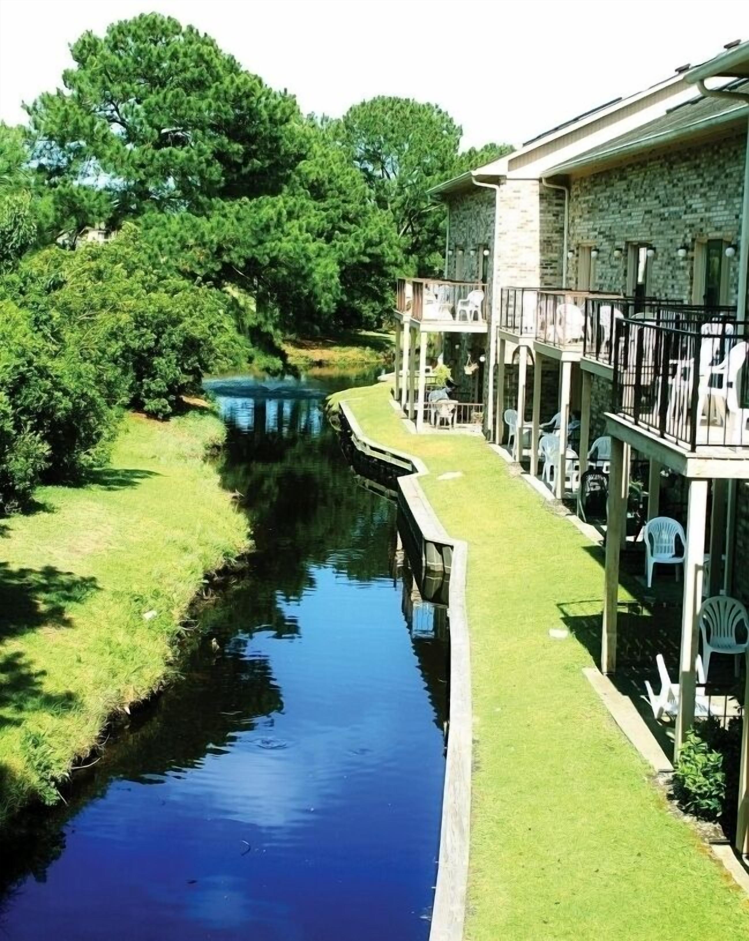 Un hotel junto al río con una terraza cubierta de césped, asientos al aire libre y un edificio de piedra.