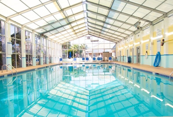 An indoor swimming pool with clear glass walls, a tiled floor, and a roof supported by metal beams. - Myrtle Beach | Group Beach Retreat | Pool + Hot Tub | 3BR Sleeps 12 (Surfside Beach)