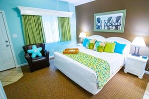 Een hotelkamer met een bed, een stoel, een nachtkastje, een lamp en een raam met gordijnen.