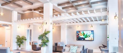 Un vestíbulo amplio con techo alto, vigas de madera, una pantalla de televisión grande y una zona de estar con mobiliario de mimbre.