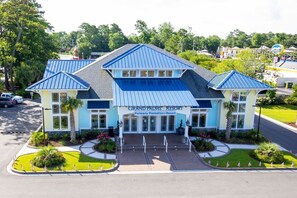 A hotel with a blue roof, a sign reading 'Grand Palms Resort,' and a landscaped entrance with American flags. - Myrtle Beach | Group Beach Retreat | Pool + Hot Tub | 3BR Sleeps 12 (Surfside Beach)