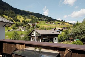Ein Balkon mit Tisch und Stühlen mit Blick auf ein Dorf mit traditionellen Häusern und einem Berg im Hintergrund.