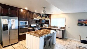 A modern kitchen with dark wood cabinets, stainless steel appliances, and a central island with stools. - Simi Valley Pool Home Spacious & Fully Furnished 4bd 2ba (Simi Valley)