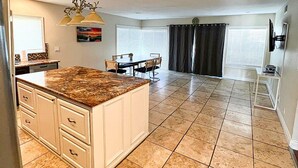 A spacious kitchen with a large island, a dining area with chairs, and a TV mounted on the wall. - Simi Valley Pool Home Spacious & Fully Furnished 4bd 2ba (Simi Valley)